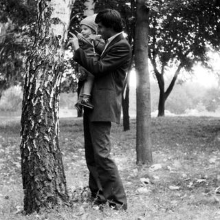A man holding a child takes a photo outdoors.
