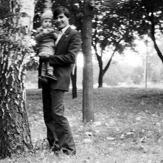 A man in formal attire holding a baby outdoors.