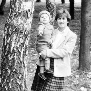 Woman holding young child outdoors near trees.