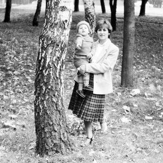 Woman holding young child outdoors near trees.