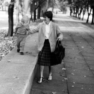 A woman holding a toddler walks outdoors.