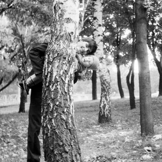 Child hugging tree trunk in park.