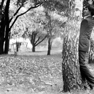 A man holding a baby near a tree.