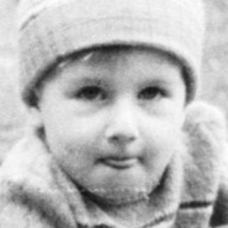 Young child sitting outdoors on grass with suitcase.