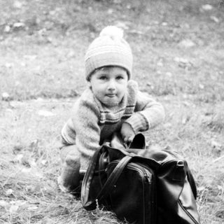 Young child sitting outdoors on grass with suitcase.
