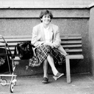 A woman sits on a bench with a stroller, a child holds a small dog on a leash.