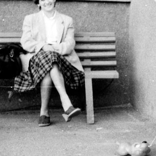 A child walks a small dog while an adult sits nearby.