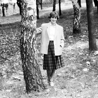 Woman standing outdoors near tree in 1960s-style attire.