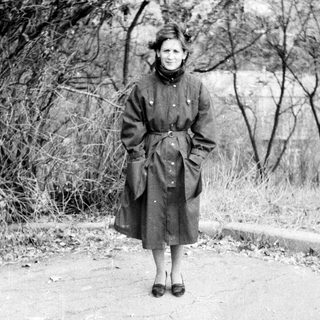 Woman in vintage coat standing outdoors on path.