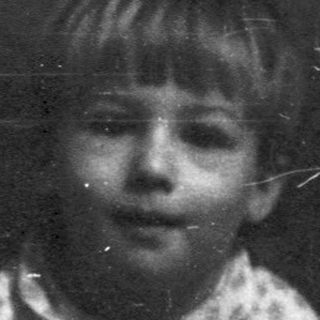 Young child sitting indoors, looking thoughtful.