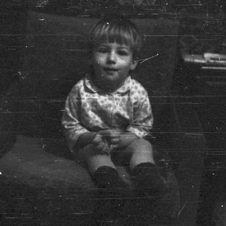 Young child sitting indoors, looking thoughtful.
