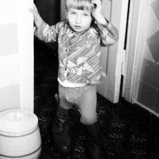 Young child standing indoors near bucket.