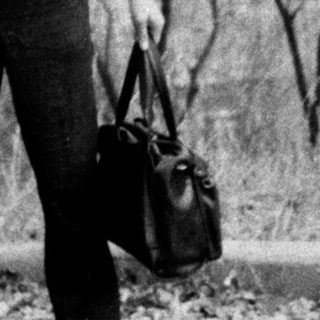 Young man standing outdoors with suitcase.