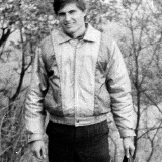 Young man standing outdoors with suitcase.