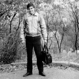 Young man standing outdoors with suitcase.