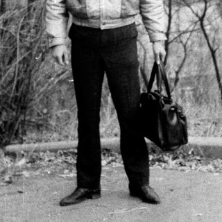 Young man standing outdoors with suitcase.