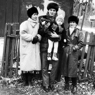Family posing outdoors in winter clothing, holding a child.