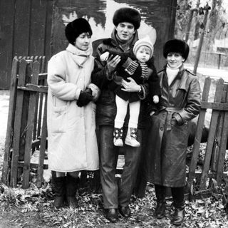 Family posing outdoors in winter clothing, holding a child.