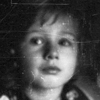 Child holding stuffed animal in dim lighting.