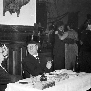 Two elderly men in formal attire smoking indoors.
