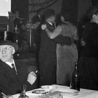Two elderly men in formal attire smoking indoors.