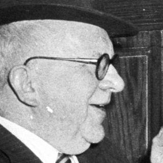 Two elderly men in formal attire having a meal together indoors.