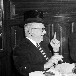Two elderly men in formal attire having a meal together indoors.