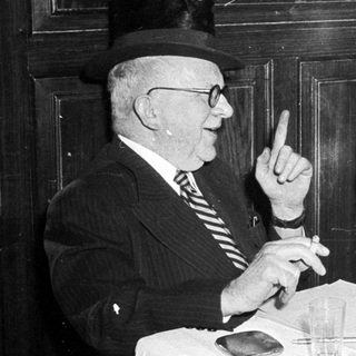 Two elderly men in formal attire having a meal together indoors.