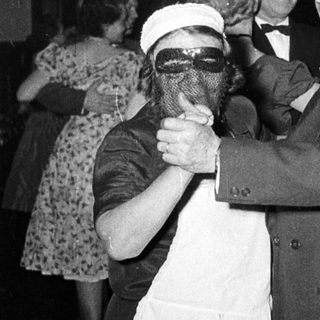 Man in suit dancing with masked woman at formal event.