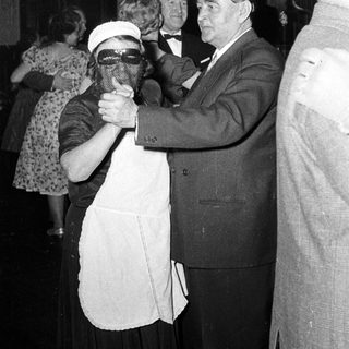 Man in suit dancing with masked woman at formal event.