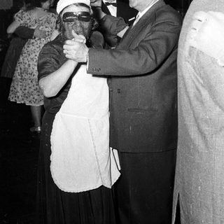 Man in suit dancing with masked woman at formal event.