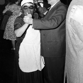 Man in suit dancing with masked woman at formal event.