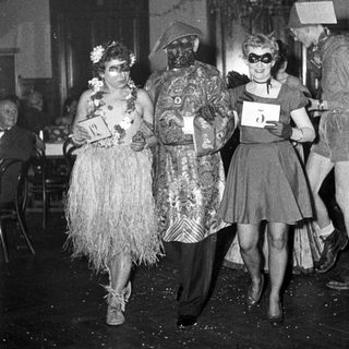 Costumed party attendees in 1940s-style masks and themed outfits.