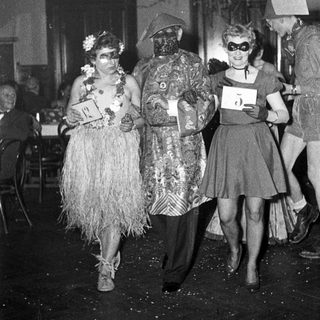 Costumed party attendees in 1940s-style masks and themed outfits.