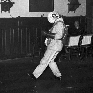 Person in white mask dancing indoors at nighttime event.