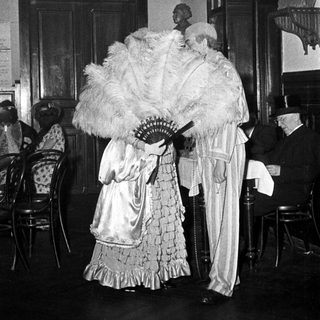 Elegant 19th-century formal attire with fans indoors.