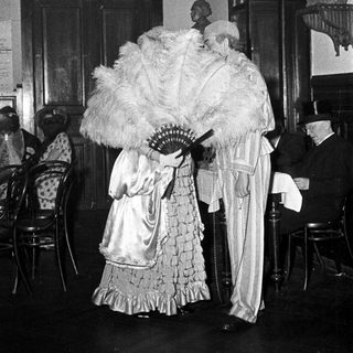Elegant 19th-century formal attire with fans indoors.