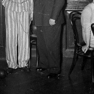 Prisoner in striped uniform holding gallows prop.
