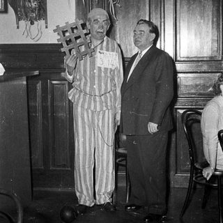 Prisoner in striped uniform holding gallows prop.