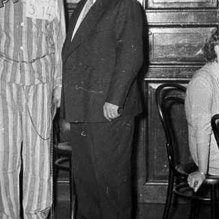 Prisoner in striped uniform holding gallows prop.