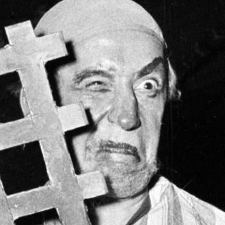 Prisoner in striped concentration camp uniform holding bar.