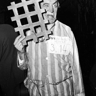 Prisoner in striped concentration camp uniform holding bar.