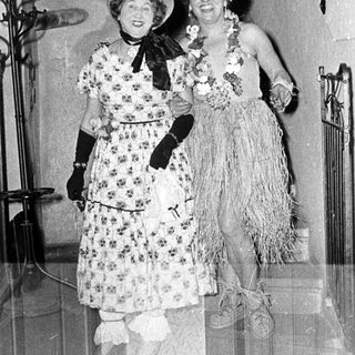 Two women in vintage Hawaiian-themed costumes posing indoors.