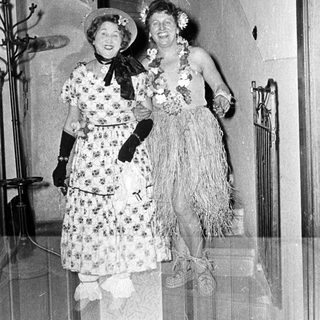 Two women in vintage Hawaiian-themed costumes posing indoors.