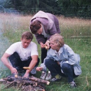 Three people roasting marshmallows over a campfire outdoors.