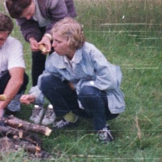 Three people roasting marshmallows over a campfire outdoors.