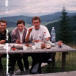Three people picnicking outdoors with food and drinks.
