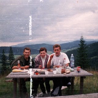 Three people picnicking outdoors with food and drinks.
