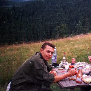 Three people picnicking outdoors on grassy hillside.
