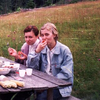 Three people picnicking outdoors on grassy hillside.